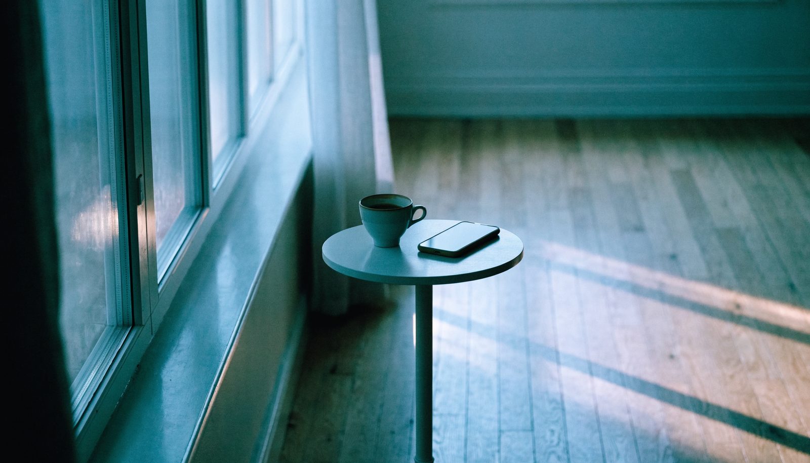 Tasse de café froide et téléphone posé face contre table au petit matin, consulter trop souvent
