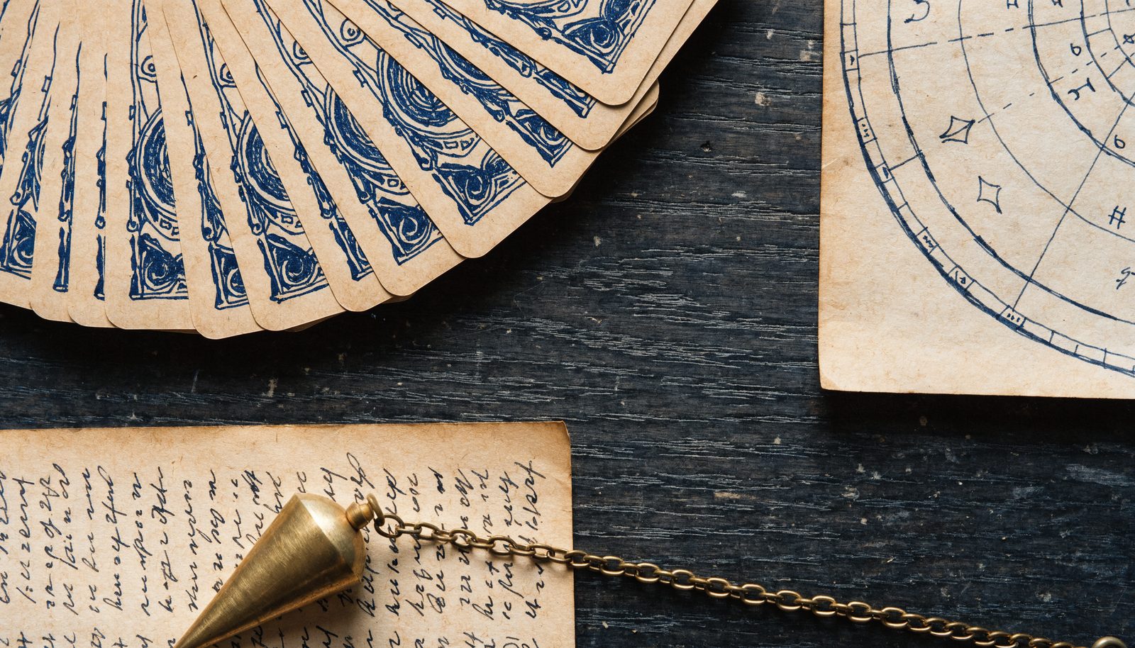 Jeu de tarot, thème astral manuscrit et pendule posés côte à côte, les outils du médium, du tarologue et de l'astrologue